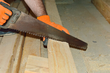 man in orange protective gloves saws a wooden board with a hand saw at a construction site