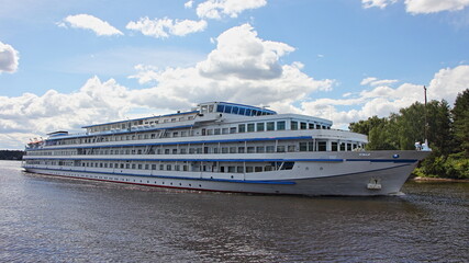 Beautiful big long four deck white cruise ship floating on the river on a summer day on blue sky with clouds background, river cruises in Russia tourism