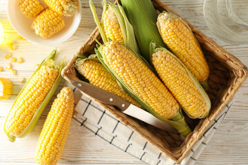 Composition with fresh corn and oil on white wooden background, top view