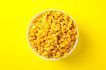 Bowl of fresh corn on yellow background, top view