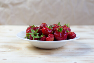 White plate with ripe red fresh strawberry on wooden table