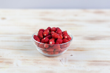 Ripe forest strawberry in glass bowl on wooden baclground