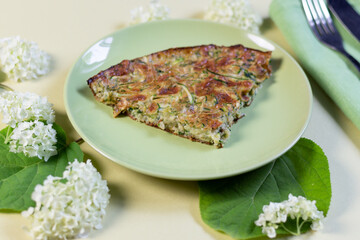 Squash casserol on  plate with fork and knife on textile on green background with hydrangea flowers