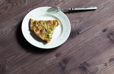 Squash casserol on white plate with fork on brown wooden background