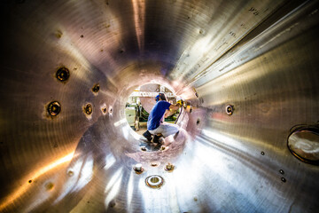 Welder at work inside a huge metal pipe in industrial environment