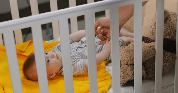 father holding baby bottle and feeding cute infant boy in baby crib
