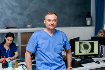 Selective focus on doctor in blue scrubs. Leaning on table in office.