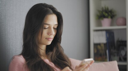 Woman sitting on a couch using her mobile phone to text a friend.