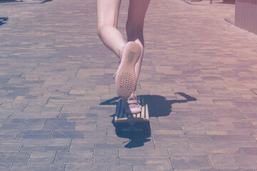Teen girl rides on a skateboard in a city park. Female legs in sneakers closeup. Bright vintage photo