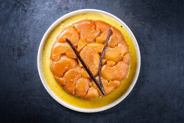Traditioneller französischer Tarte Tatin Kuchen mit Äpfel und Vanille angeboten als Draufsicht auf einem Modern Design Teller mit rustikalen Hintergrund