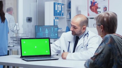 Doctor talking near a laptop with green screen and elderly patient looking at it. Mockup mock-up isolated background ready to be removed chroma key keying for your app or advertisement