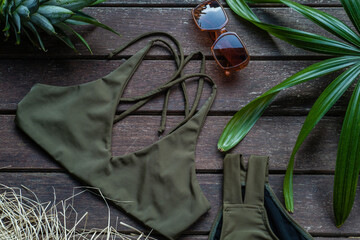 Top view of green bikini swimsuit swimwear with beach accessories on rustic wooden background. Summer vacation concept. Flat lay