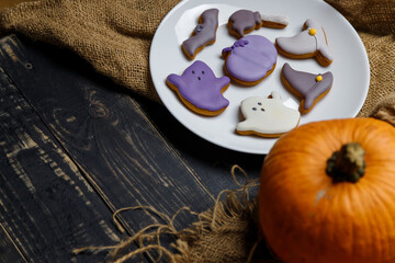 Pumpkin and Halloween cookies on white plate, sackcloth on black wooden background. Hallooween trick or treat concept. Copy space.