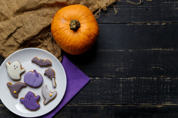 Obraz na płótnie Canvas Pumpkin and Halloween cookies on white plate, sackcloth on black wooden background. Hallooween trick or treat concept. Copy space.