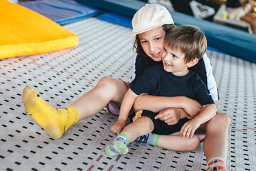 Funny smiling kids on trampoline. Older brother embraces younger. Active rest in the sport center. Two happy emotions boys, brothers playing and having fun while jumping on trampoline