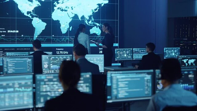 Project Manager and Computer Science Engineer Talking while Using Big Screen Display Showing Global Map and Data. Telecommunications Company System Control and Monitoring Room.