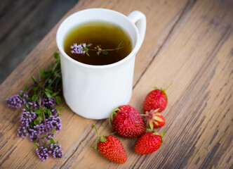 White tea Cup with grass thyme and strawberries on a wooden background top view