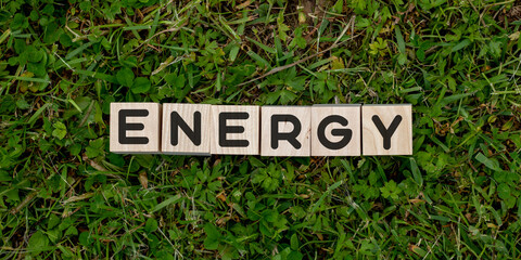 The word energy is written on wooden blocks on a background of grass. View from above. Banner. The concept of energy conservation or eco-friendly methods of energy production.