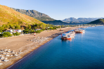 Fototapeta premium Long beach coast, dark teal sea and bay in Adrasan village Mediterranean coast, great place for holiday. Excursion boats on the beach. Aerial view with drone. Antalya, TURKEY