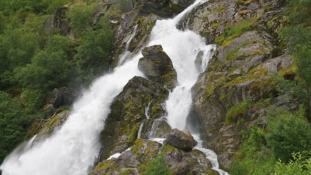 Panoramic view to Kleivafossen waterfall on Briksdalselva river, Briksdalsbreen glacier, Norway. Waterfall on the way to Briksdal or Briksdalsbreen glacier in Olden, Norway and green mountains.