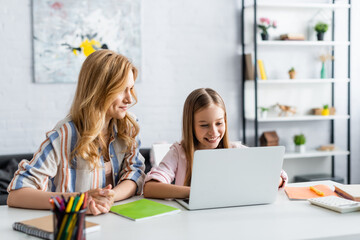 Selective focus of smiling kid using laptop near mother during online education