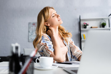 Selective focus of exhausted woman touching neck while working at table