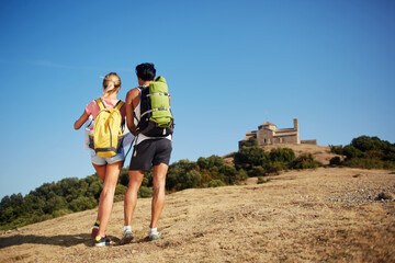 Naklejka premium Back view of a two backpackers are exploring location map while standing on a high hill against beautiful blue sky, man and woman wanderers are walking together in mountains during their summer trip