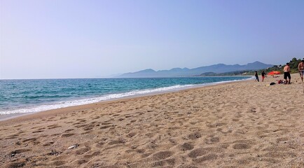 Fototapeta na wymiar People enjoying a long stretch of sandy beach in Greece