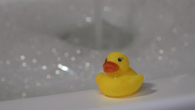 Yellow rubber plastic duck sits on the side of the bath. In bathroom.