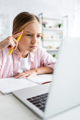 Selective focus of focused kid holding pen and looking at laptop