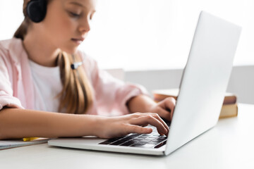 Selective focus of kid in headset typing on laptop at home