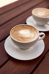 Two cups of cappuccino on the wooden background. Beautiful brown foam, white ceramic cups, place for text