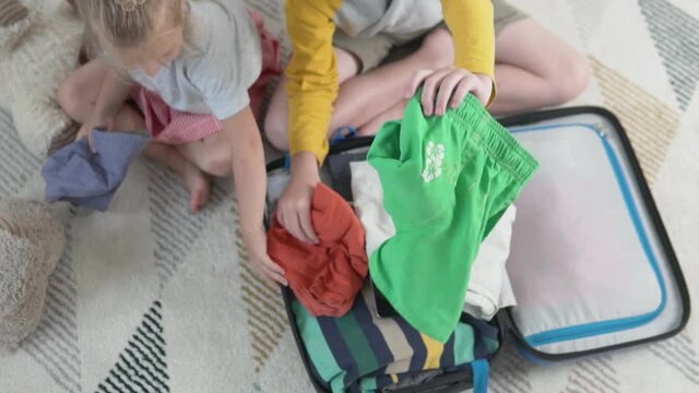 The children are packing their bags on holiday. A boy and a girl put their clothes in a suitcase in a children's room. Preparing for travel