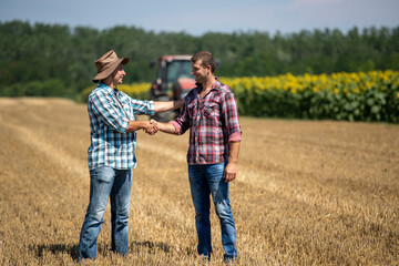 Naklejka na ściany i meble Farmers shaking hands in field during harvest