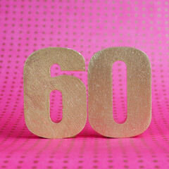 Golden volumetric number 60 on a bright pink polka dot background. copy space..