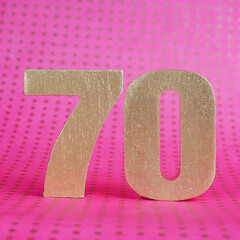 Gold volumetric number 70 on a bright pink polka dot background. copy space..