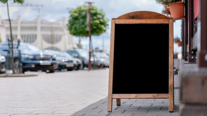 empty black chalkboard in wooden frame stands near street cafe entrance for menu information