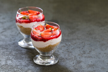 Dessert cheesecake with cookies, cream cheese, strawberry sauce and strawberry slices in a glass on a dark gray background