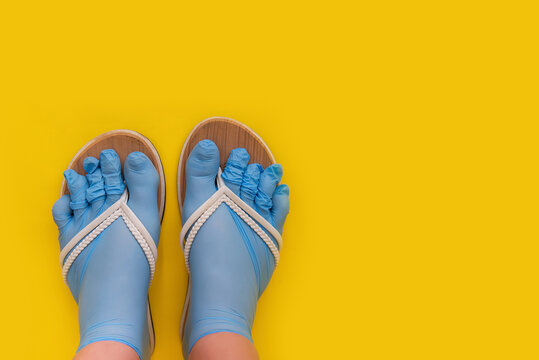 Legs of a girl dressed in rubber blue medical sterile gloves, shod in white flip flops on an orange yellow plain background. A joke of a safe rest on the sea in the sand, protection against a virus