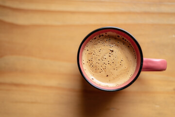 Pink cup with freshly made coffee resting on a wooden table