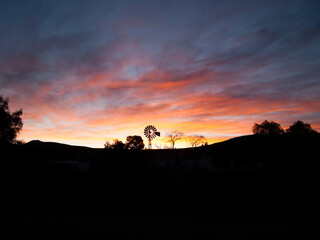 Fototapeta na wymiar Dramatic sunset on remote farm with wind pump