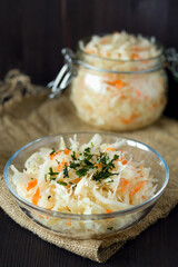 homemade sauerkraut with carrots with herbs in glass jar on a black background.Pickled cabbage on the plate with sackcloth on the wooden table. copy space. The concept of canned food. vegetarian food.