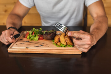 emotional young man sitting at the table, waiting to eat, in front of her is a steak with french fries and a salad of greens