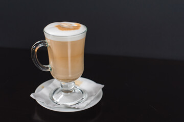 Coffee latte macchiato in a tall glass on a dark wooden background. There is space for copying next to the glass, and the photo is horizontal
