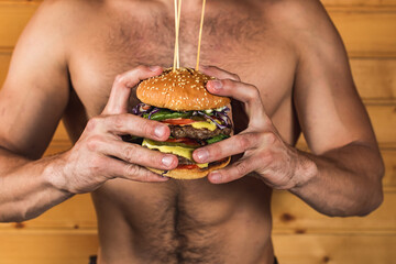 Young sympathetic man holding fast food burger in his hands, American unhealthy calorie food on background, layout space for text message or design, hungry man smiling with fried hamburger front view 
