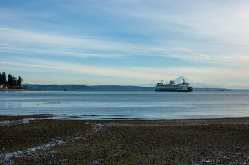 Ferry in Puget Sound against the backdrop of Mount Rainier, with blue sky and some clouds, as seen from Hawley Cove on Bainbridge Island