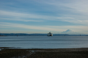 Obraz premium Ferry in Puget Sound against the backdrop of Mount Rainier, with blue sky and some clouds, as seen from Hawley Cove on Bainbridge Island