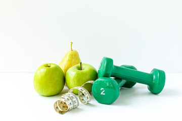 Green apples, dumbbells and a twisted centimeter ribbon on a white background. The concept of a...
