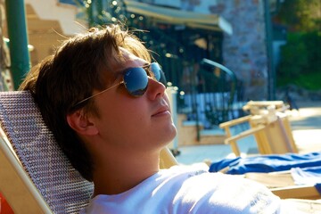 a handsome man is lying on a sunbed on the beach with glasses