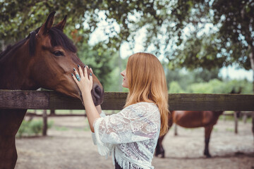 Woman in fashionable Bohemian casual style with horses on a farm, pets animals in village at rancho. Horses are human friends